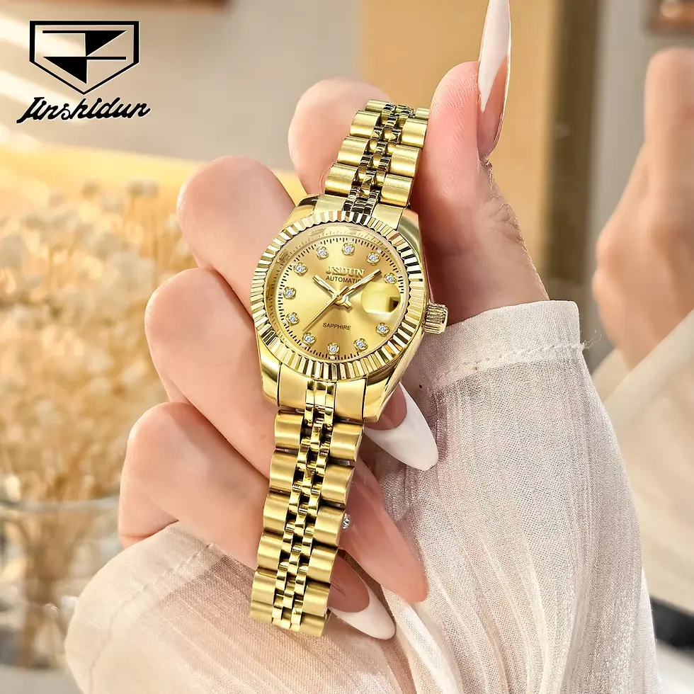 Hand holding a gold watch with a jeweled face and linked band, set against a blurred warm background.