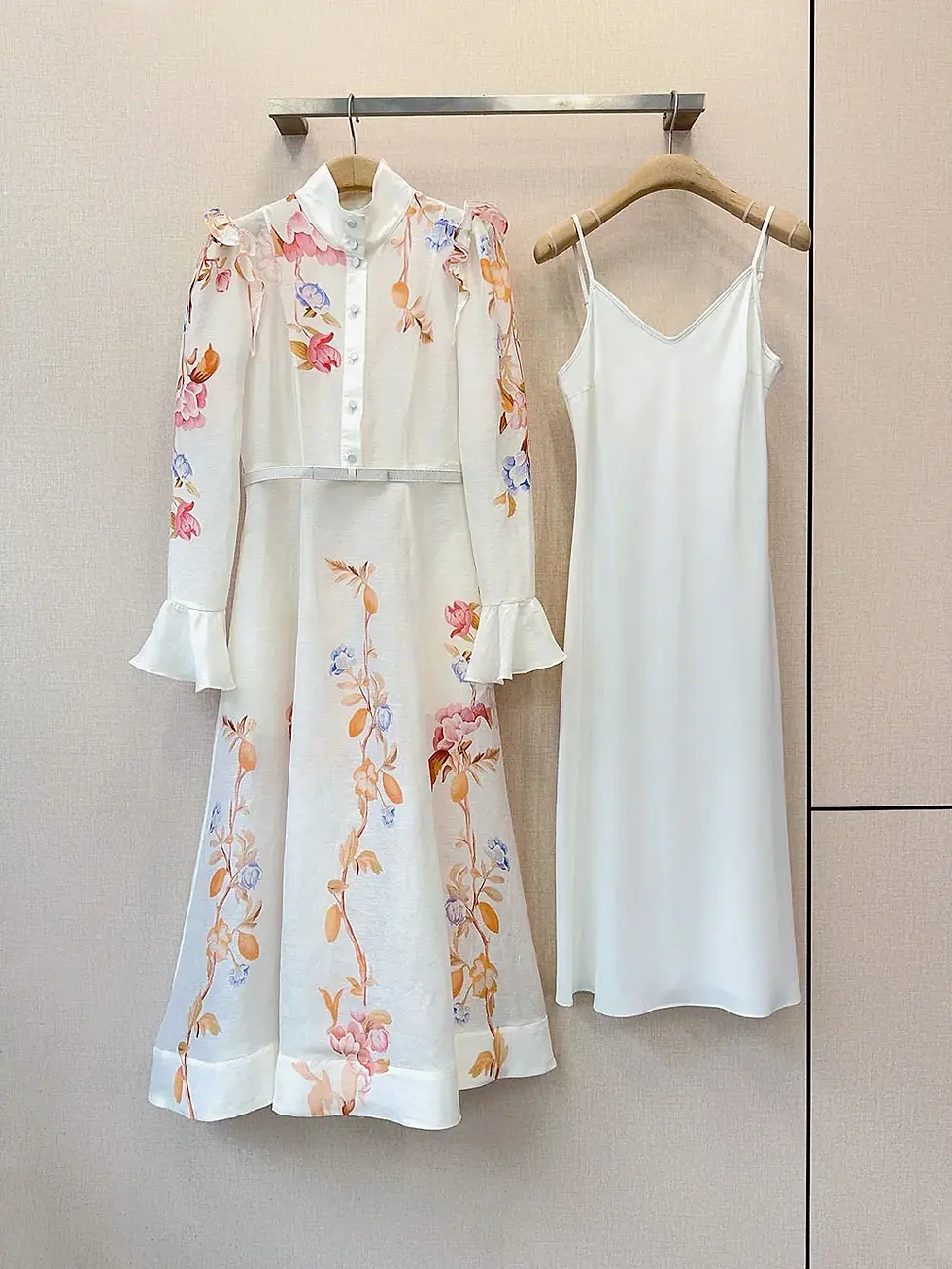 Floral long-sleeve dress with ruffle details and a white slip dress on hangers.