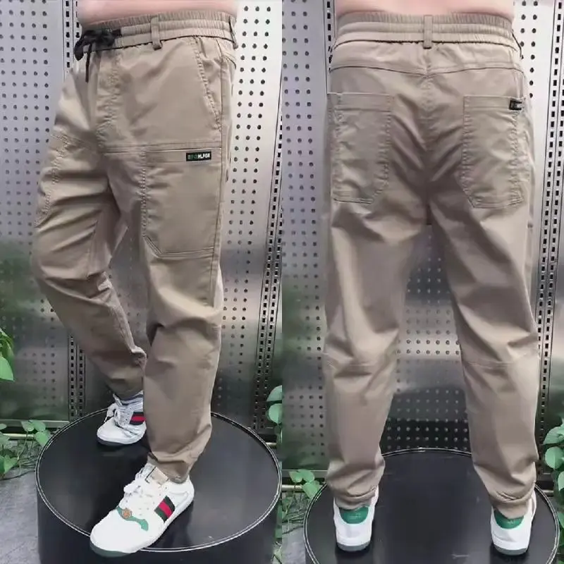 Miniaturebillede: Gray cargo pants displayed from front and back on a model wearing white sneakers and a shirt, with a striped background.