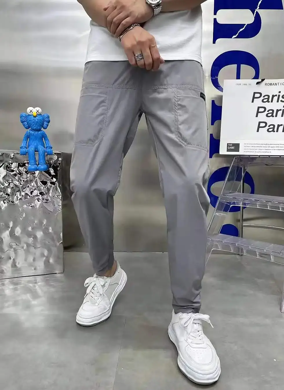 Thumbnail: Gray cargo pants displayed from front and back on a model wearing white sneakers and a shirt, with a striped background.