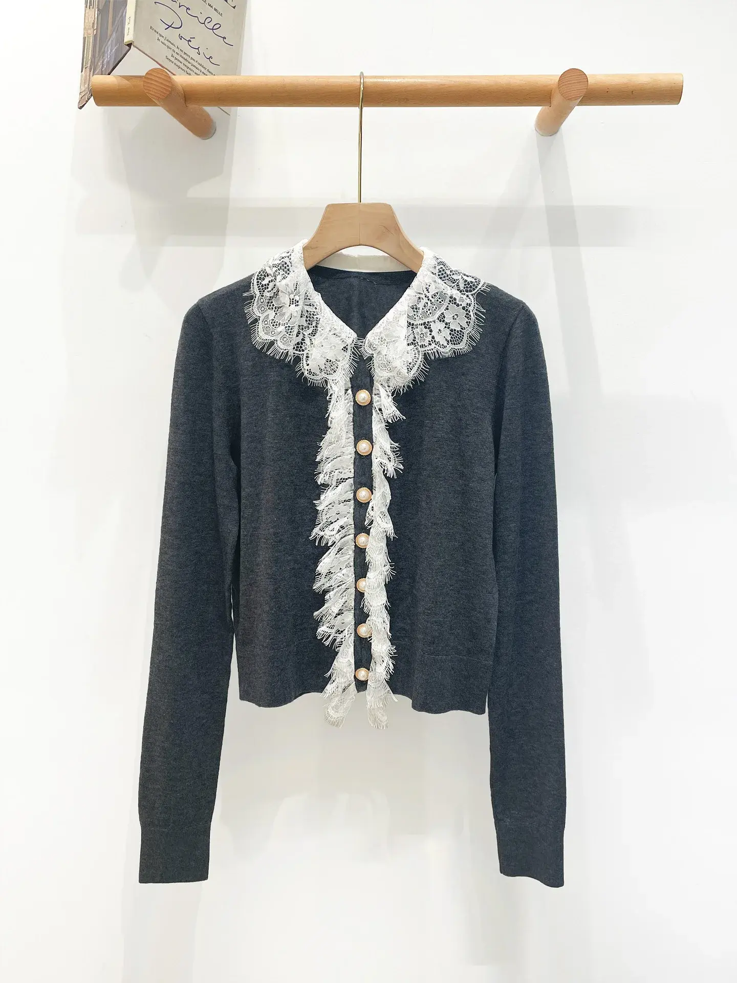 Dark sweater with white lace collar and gold buttons, hanging on a wooden hanger against a white wall.