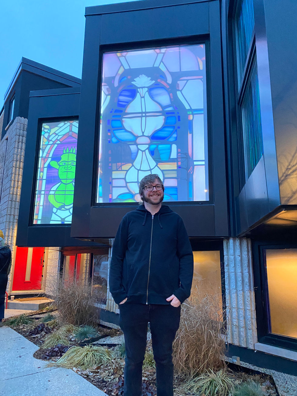 The artist Ryan Cranfill (AKA Scholastic Rodent) in front of his installation of AI-enabled stained glass windows