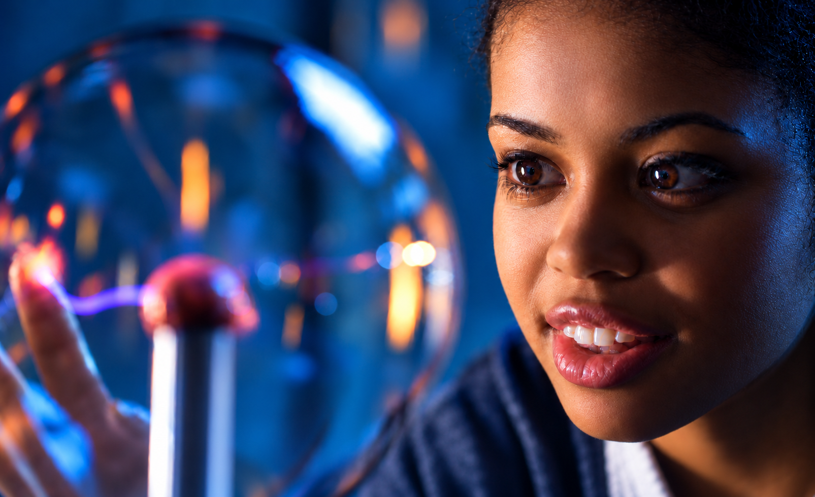 A young woman looks into a glowing plasma globe, lit in blue and orange