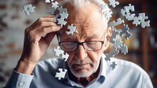 Elderly man in glasses holds his head as puzzle pieces float around him, suggesting confusion or memory loss in a soft-lit room
