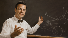 Richard Feynman in white shirt and bow tie gestures at chalkboard covered with physics diagrams.