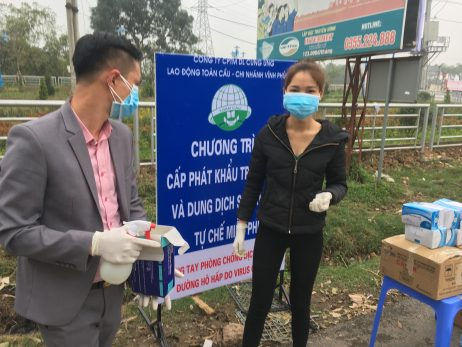 Health officials stand in front of a warning sign about the COVID-19 disease at a checkpoint before entering the Son Loi commune in Vinh Phuc province, Vietnam on Feb. 13, 2020.
