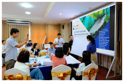 A working group at the 5 May workshop; a facilitator and others stand by a flip chart, one participant films on a phone, the project team listed on the projected slide.