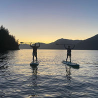 A couple with paddles in the air on SUPs at sunset - Pristine Paddleboard Adventures