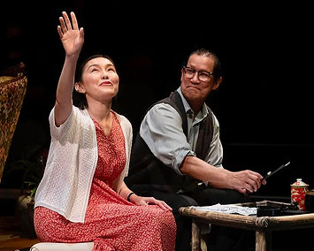 A young Chinese woman gesturing to the sky with an older Chinese man smiling
