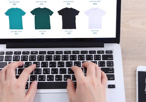 Person typing on a laptop with an eCommerce website on screen, next to a smartphone displaying the GirlDog Digital logo.