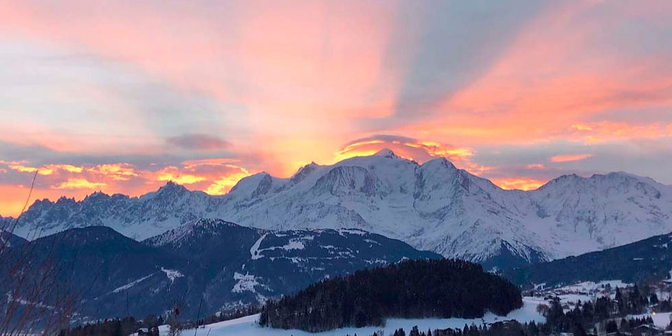 Chaîne du Mont-Blanc enneigées au lever du soleil, ciel rose et orange au-dessus d’une vallée sombre.