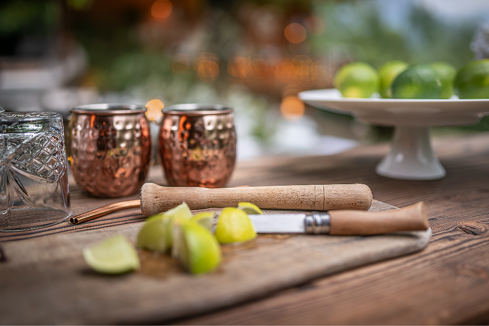 Sur une table en bois, des limes coupées, un couteau, des gobelets cuivrés et un plat blanc créent une ambiance chaleureuse.