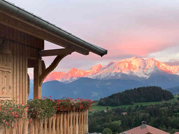 Mont Blanc bathed in pink light at sunset in Cordon. A wooden chalet balcony in the foreground, adorned with geraniums.