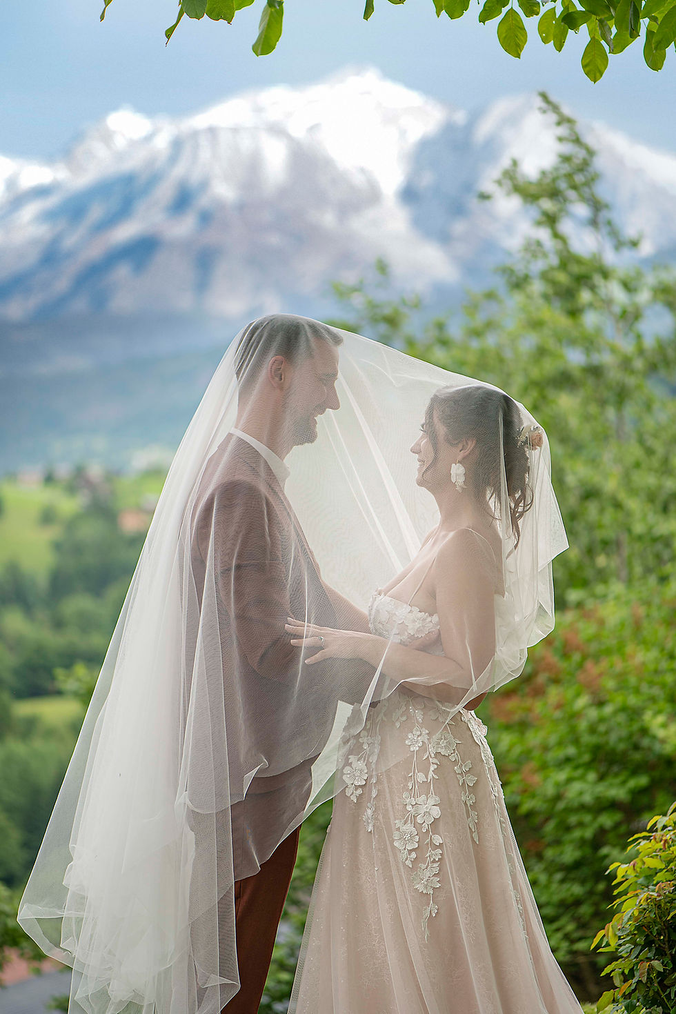 Jeunes mariés sous un voile blanc devant les montagnes