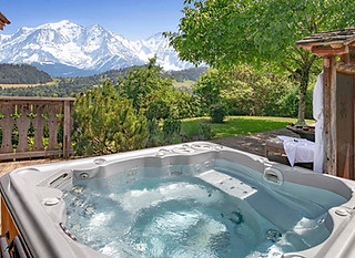 An outdoor hot tub overlooking the peaks of Mont Blanc in a summer setting.