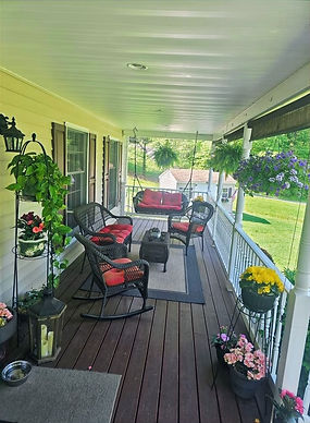Residents enjoying conversation on the sunny front porch of Front Porch Haven, surrounded by greenery and flowers.