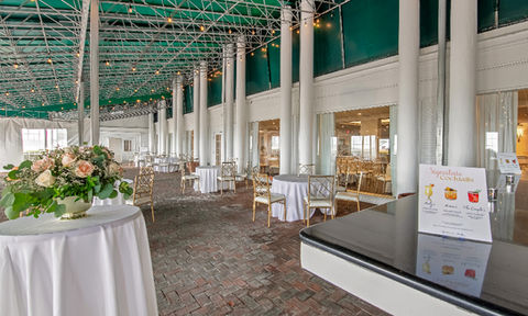 Outdoor covered patio with string lights, cocktail tables, floral decor, and visible signature drink sign.