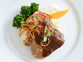 Grilled steak with mashed potatoes, broccolini, carrot, crispy onions, and gravy on a white plate.