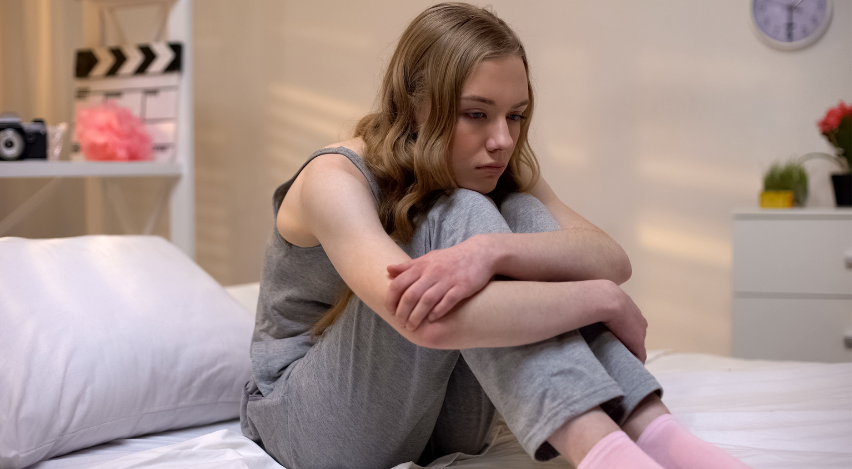 Adolescente encolhida na cama com expressão de introspecção e tristeza silenciosa