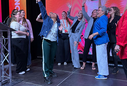 Brandi Heather stands smiling among fellow female keynote speakers at the SPARK Women’s Conference, appearing happy.