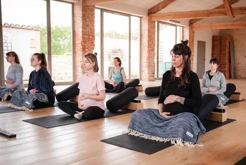 6 pregnant woman in a yoga studio sitting on their black yoga mats and bolsters (from jade) at the hummingbee retreat doing prenatal yoga and meditation.