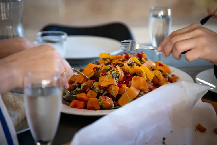 Delicious vegan dish on the table, hands grabbing some of the food with forks for their plate at dinner.