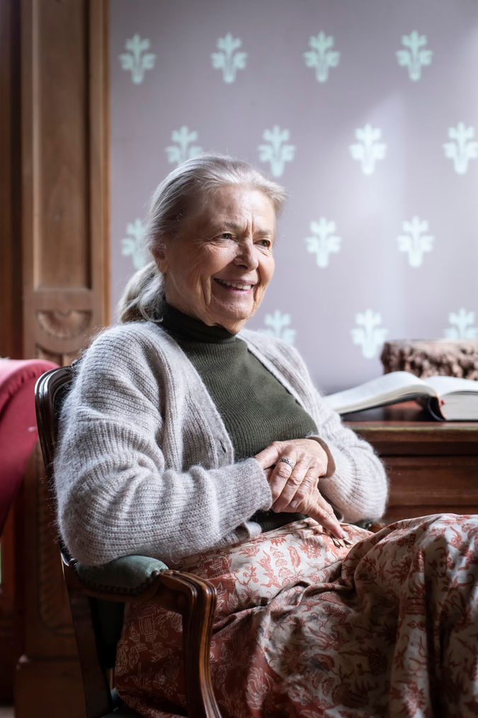 Portrait éditorial d’une femme séniore souriante assise dans un fauteuil dans un intérieur chaleureux 