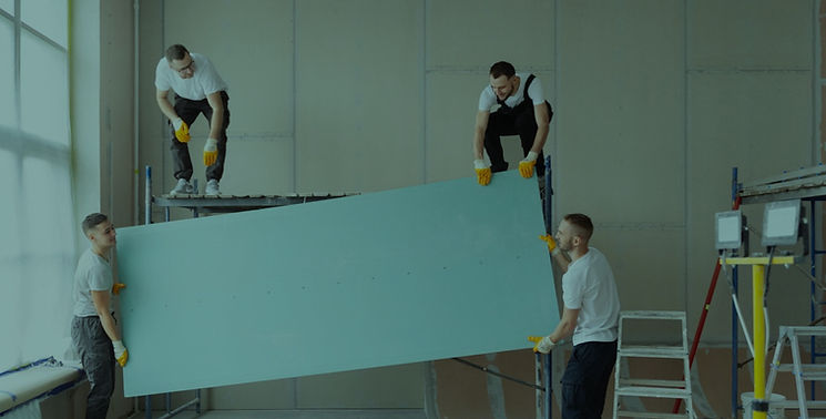 View angle view of people carrying drywall together in an industrial room