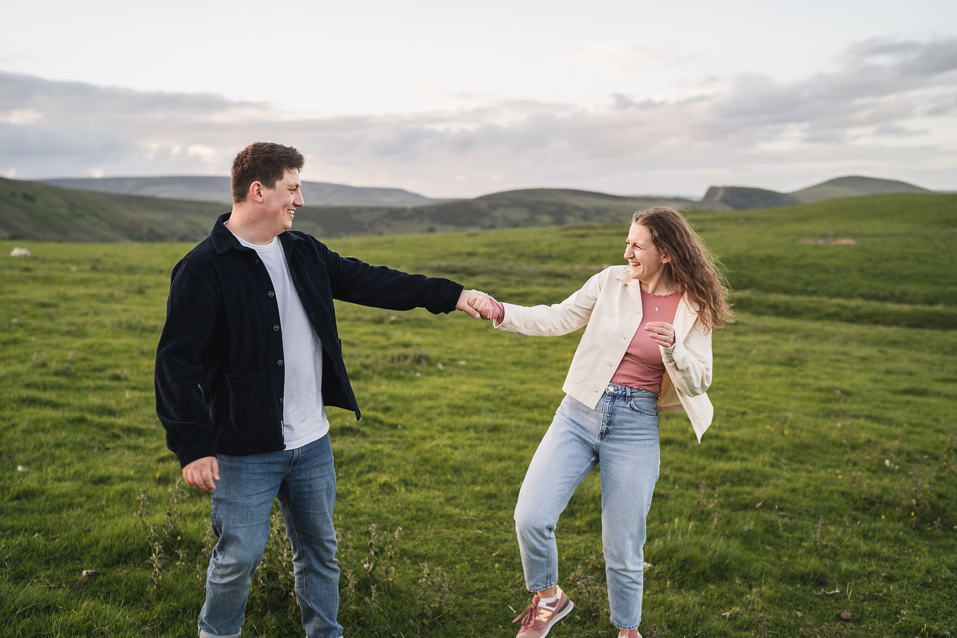 Man and woman holding hands, pulling each other about and laughing at their pre wedding shoot at Winnats Pass
