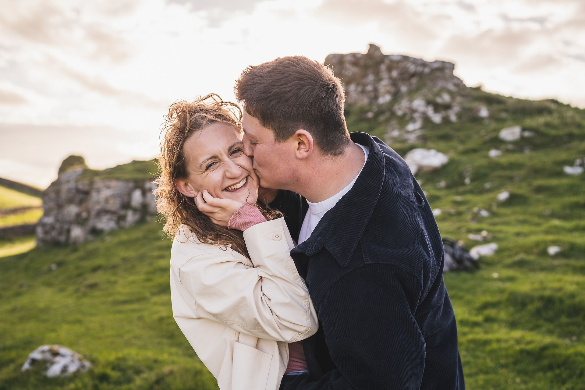 Man kissing womans cheek as she smiles at camera on their pre wedding shoot at Winnats Pass