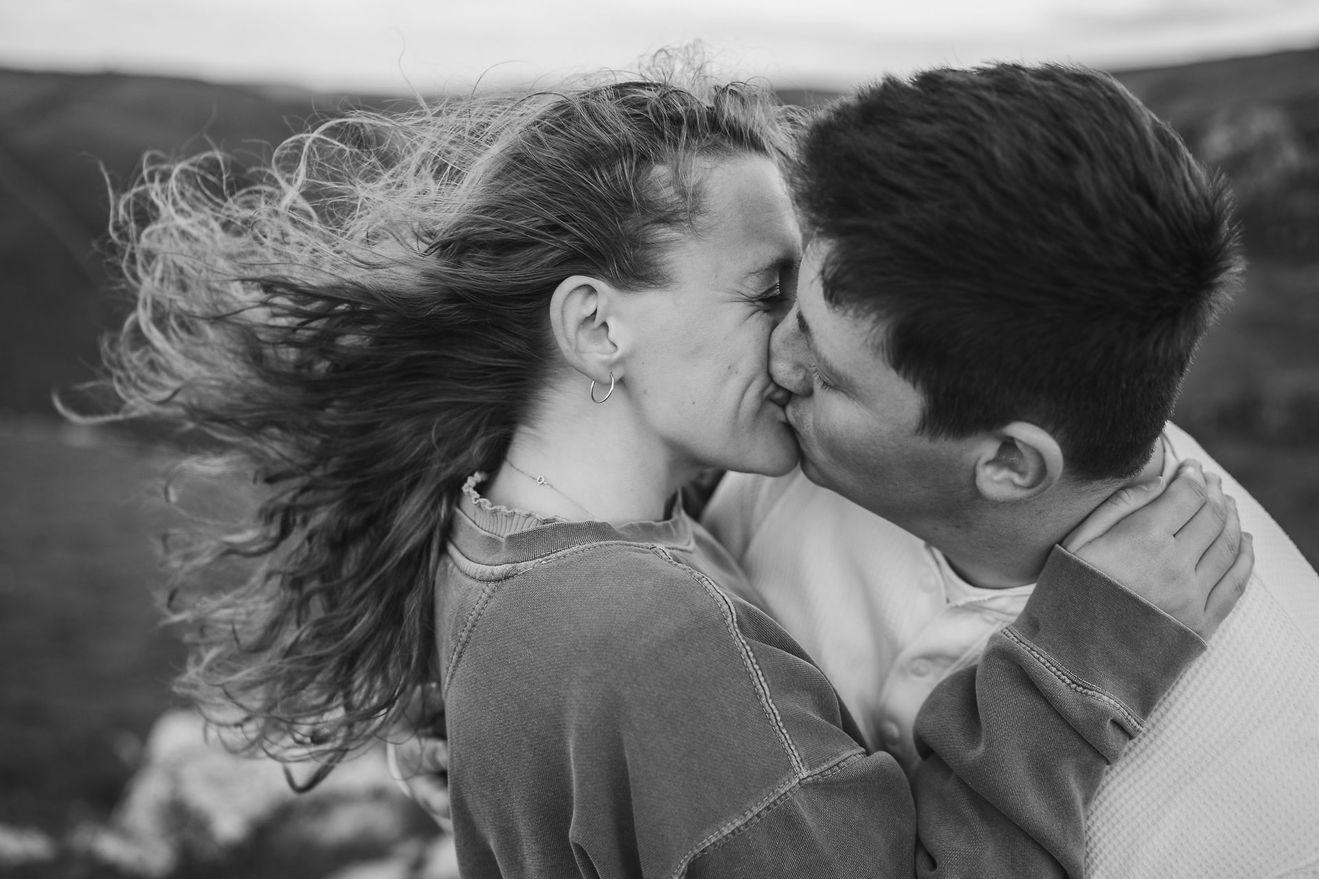 Black and white photo of couple kissing, wind blowing in their hair at the pre wedding shoot at Winnats Pass