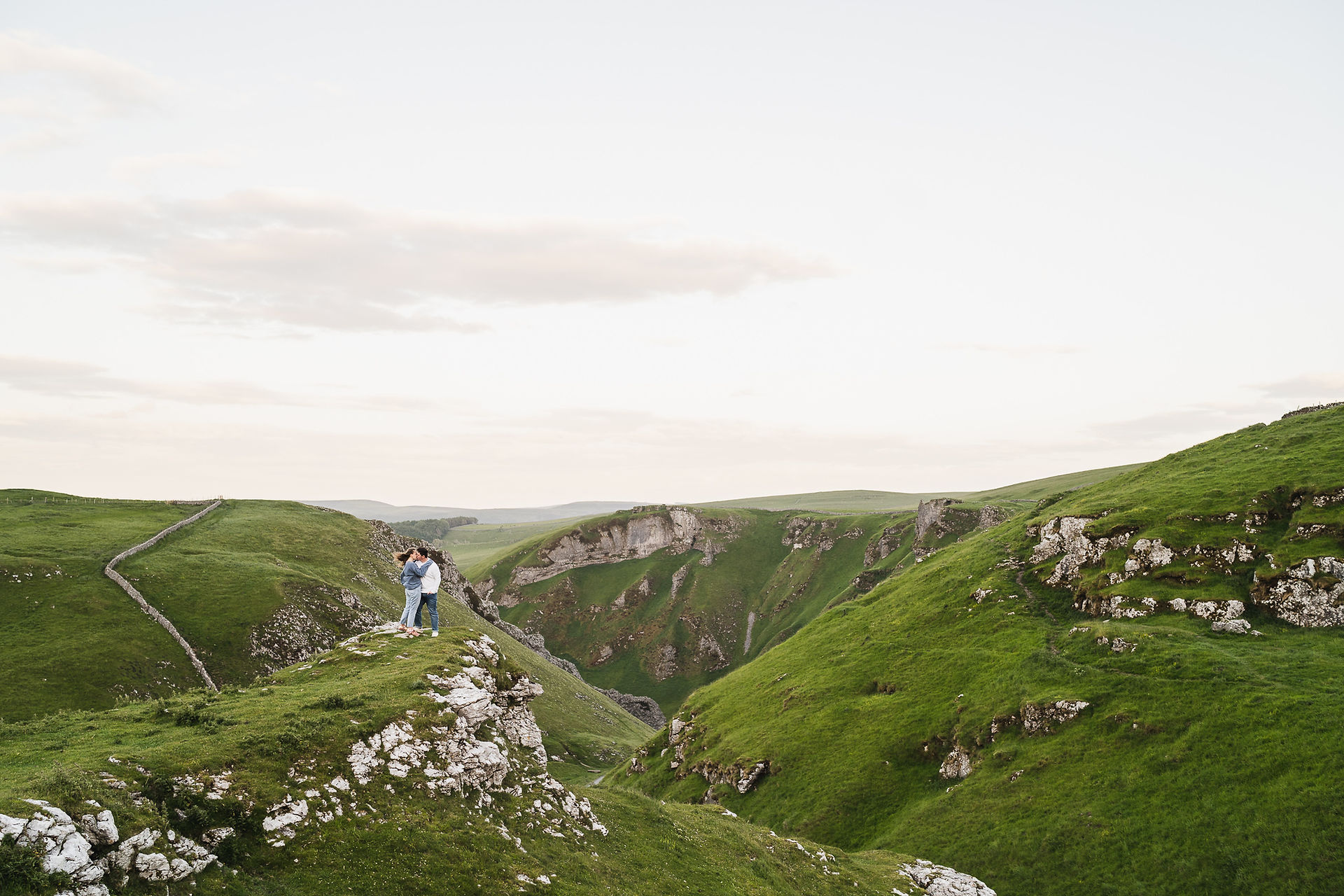 Wide shot looking down Winnats Pass with newly engaged man and woman embracing on left of shot at their Pre Wedding Shoot at Winnats Pass
