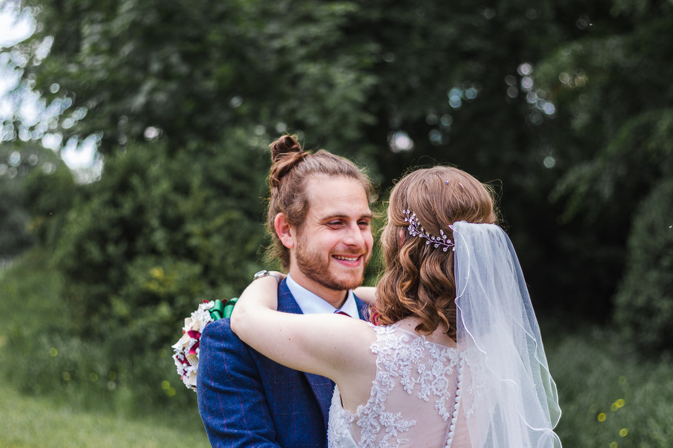 Bride with arms round grooms neck smiling at each other at Stourton Estates Wedding. photo taken from behind the bride, looking towards the groom face