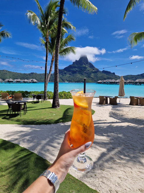 Vrouwelijke hand met cocktail met uitzicht op watervillas, lagune en wit strand