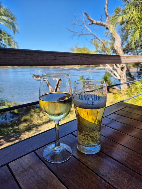 Glas witte wijn en een biertje op tafel met uitzicht op een rivier