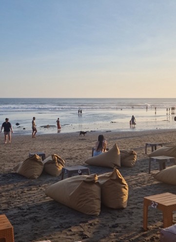 Strand in Bali tijdens zonsondergang er liggen zitzakken op het strand waar mensen zitten of lopen over het strand heen