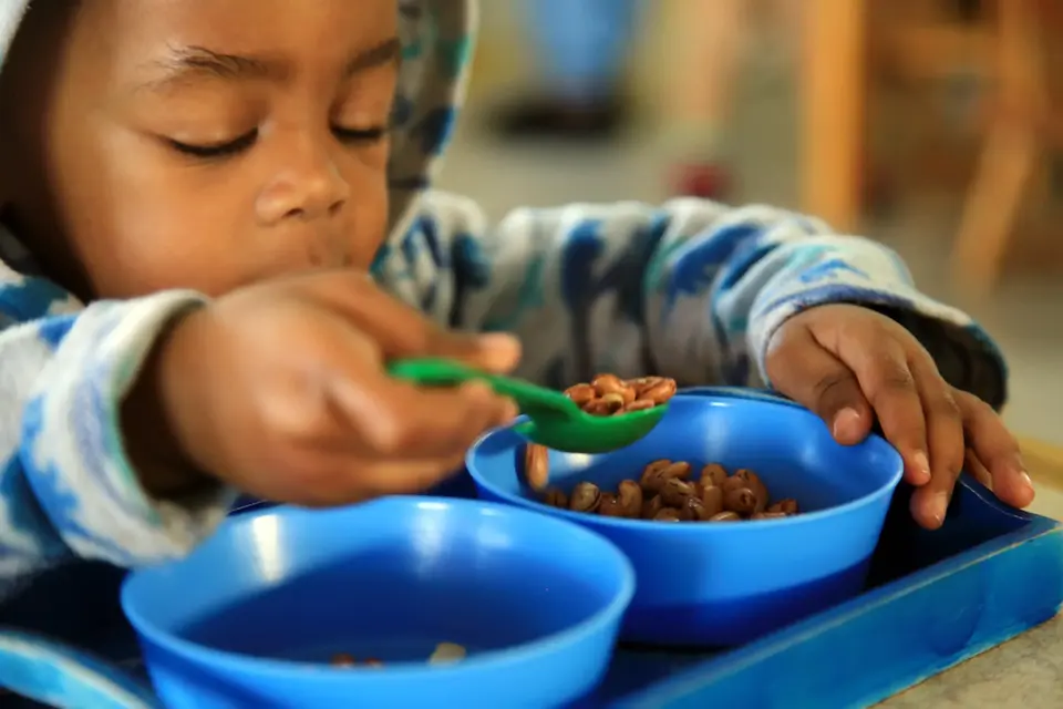 Toddler spooning beans in the Practical Life area at Midrand Montessori, building hand-eye coordination, left-to-right movement, concentration, and independence.
