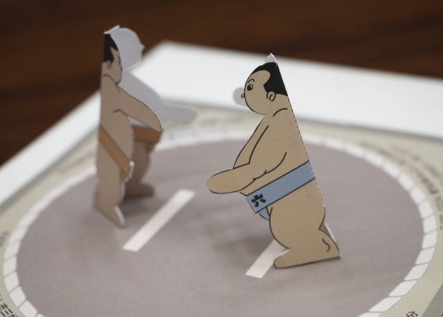 Paper figures of sumo wrestlers on a miniature ring.