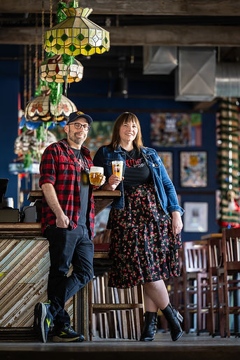 The owners of Attic Brewing Company standing at the bar with glasses of beer in their hands.