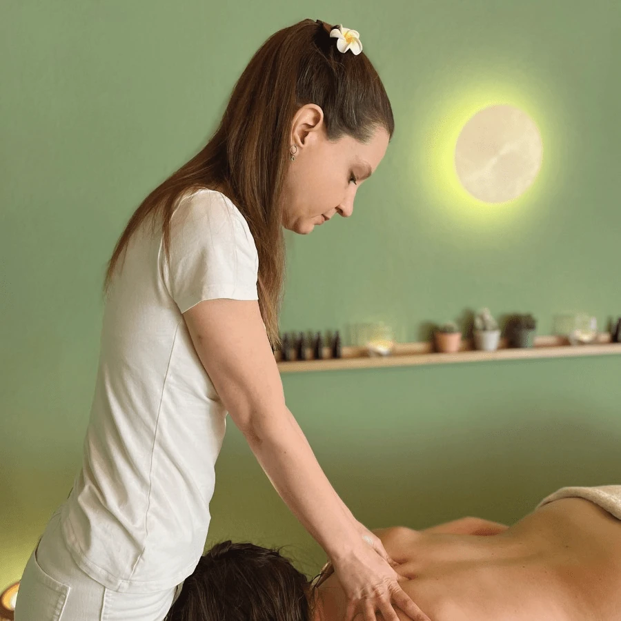 Sarah Maresch gibt eine hawaiianische inspirierte Aromaöl-Massage Behandlung mit individuellem Aromaöl in der Stressablage in Steyr. Beide Hände berühren sanft und kraftvoll zugleich den entspannten Rücken der massierten Person. Im Hintergrund sieht man die Essenzen zum Mischen der personalisierten Aromaöle.