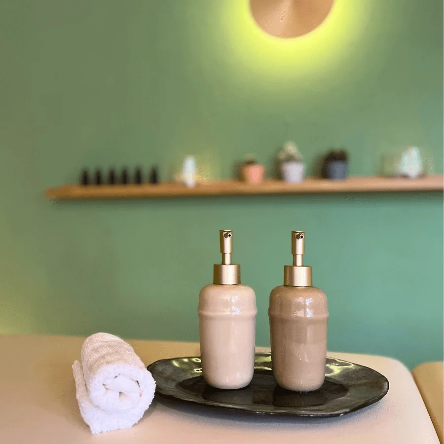 Hochwertige Stressablage-Aromaöle für die hawaiianische inspirierte Aromaöl-Massage mit weichem Handtuch auf der Massage-Liege. Im Hintergrund sieht man die Essenzen zum Mischen der personalisierten Aromaöle.