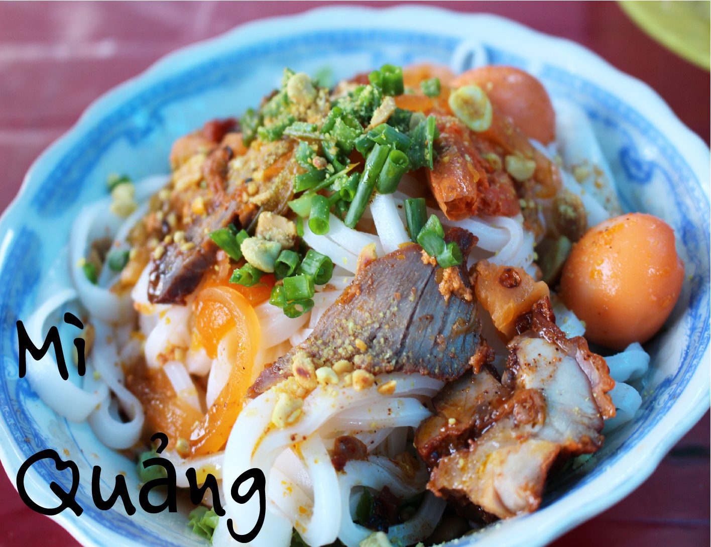 A plate of fresh herbs and chili served with a bowl of mì quảng