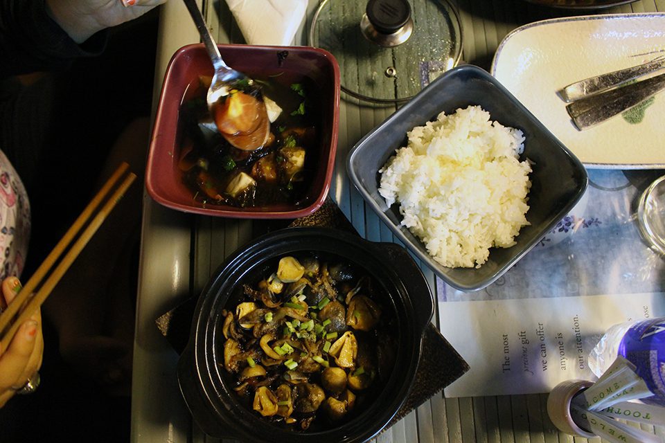 A steaming clay pot filled with mushrooms, tofu, and vegetables in a rich soy-based sauce.
