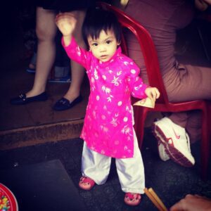 Young Vietnamese toddler dressed in a pink ao dai, celebrating Tet with family.