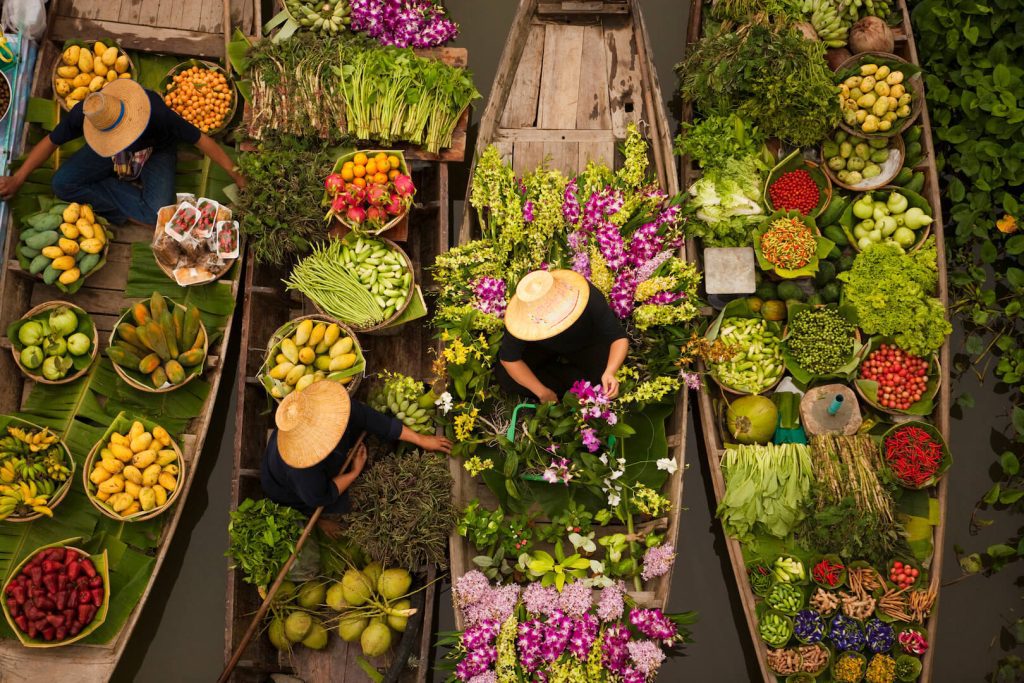 Floating market in Bangkok with boats filled with tropical fruits, vegetables, and flowers.