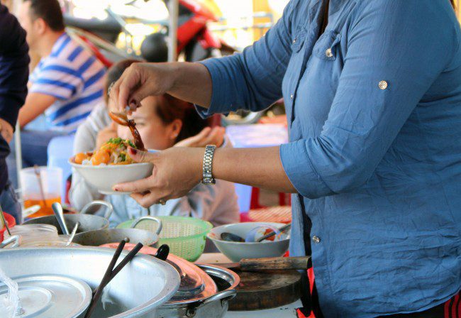 A vendor in Hoi An serving mì quảng at a street food stall.