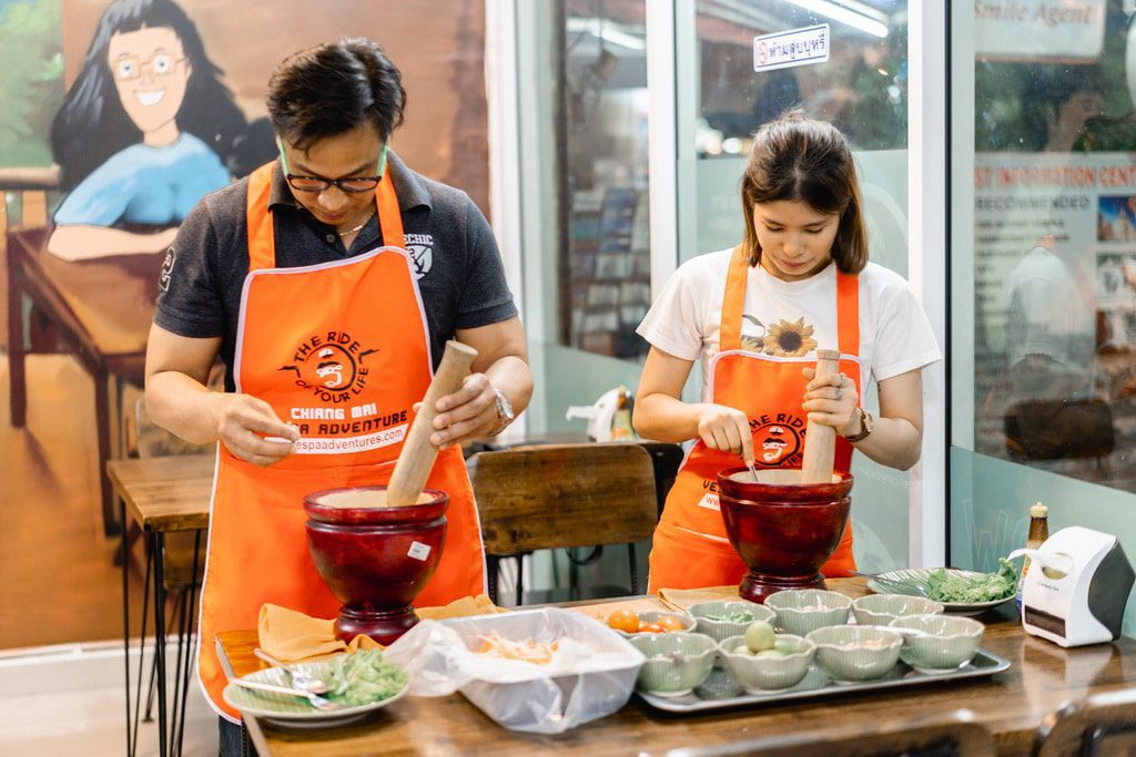 Travelers wearing orange aprons participating in a hands-on Thai cooking experience in Chiang Mai.
