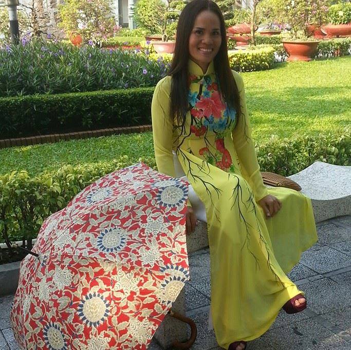 Vietnamese woman wearing a yellow ao dai with floral embroidery, standing in a lush garden.