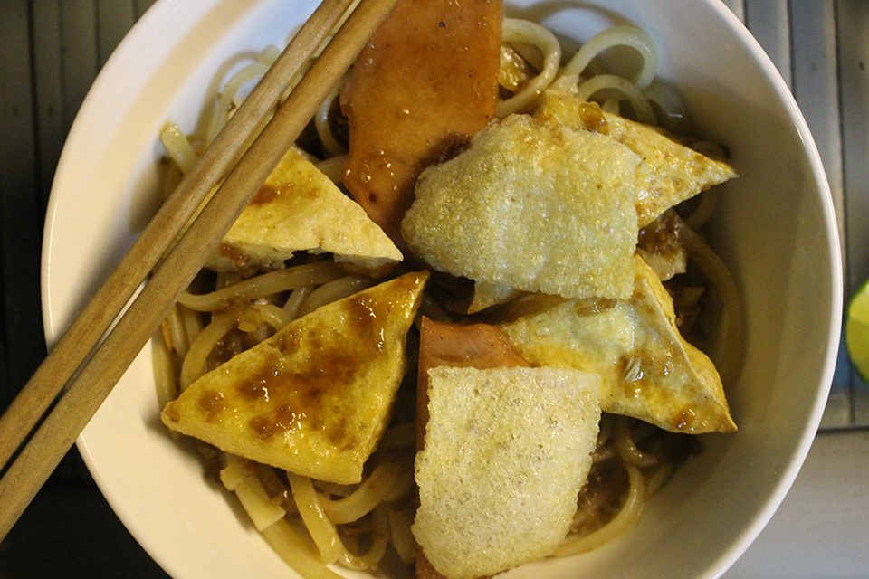 A bowl of vegetarian Cao Lau noodles with crispy tofu and rice crackers.