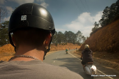View of a traveler on a Vespa scooter riding through the winding roads of Vietnam, with a scenic mountain backdrop.
